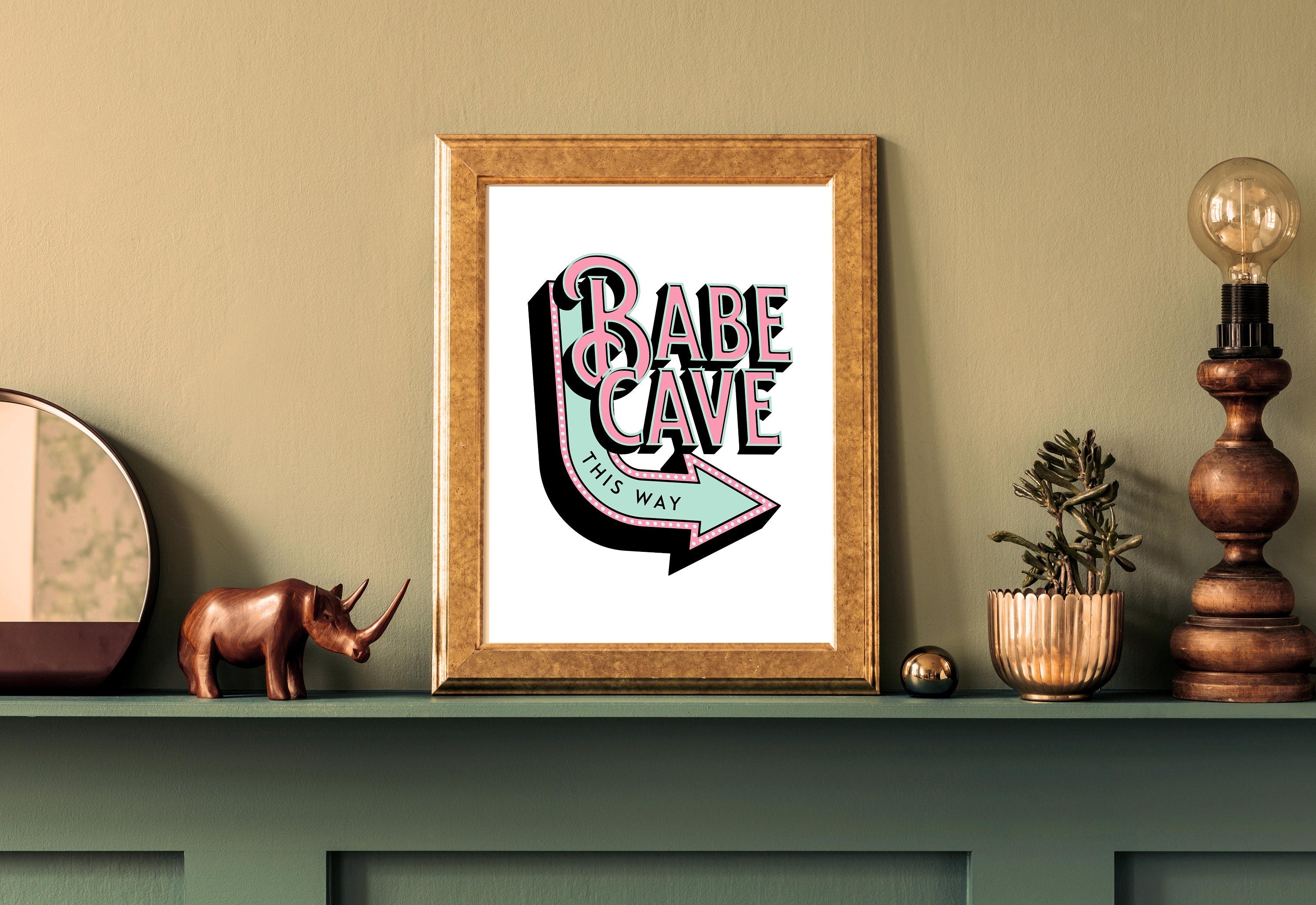 Digital art print of a chic 'Babe Cave' sign in elegant cursive against a pastel pink background.